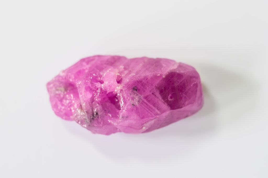A detailed macro photograph of a rich, natural Sri Lankan pink sapphire crystal displaying its deep magenta color and rough geometric texture against a dark grey background